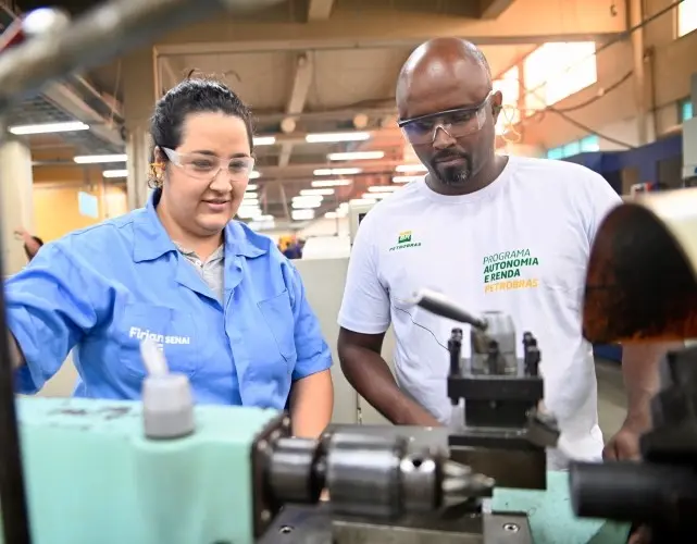 Imagem de um estudante do Programa Autonomia e Renda Petrobras do SENAI manuseando um torno mecânico ao lado da instrutora
